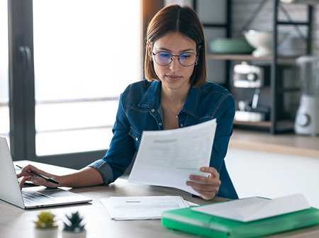 Businesswoman wearing glasses looking at paperwork with laptop