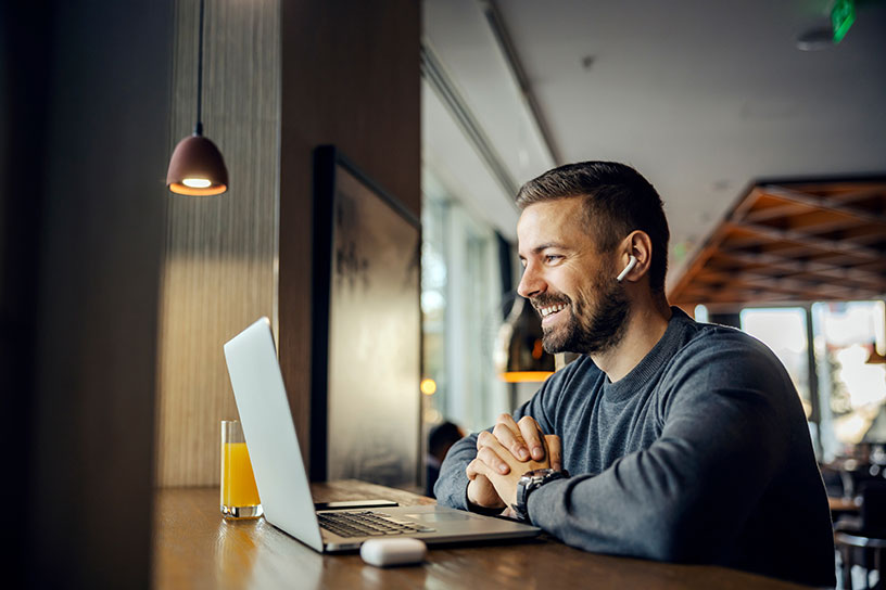 A male freelancer takes a client meeting on his laptop in a cafe