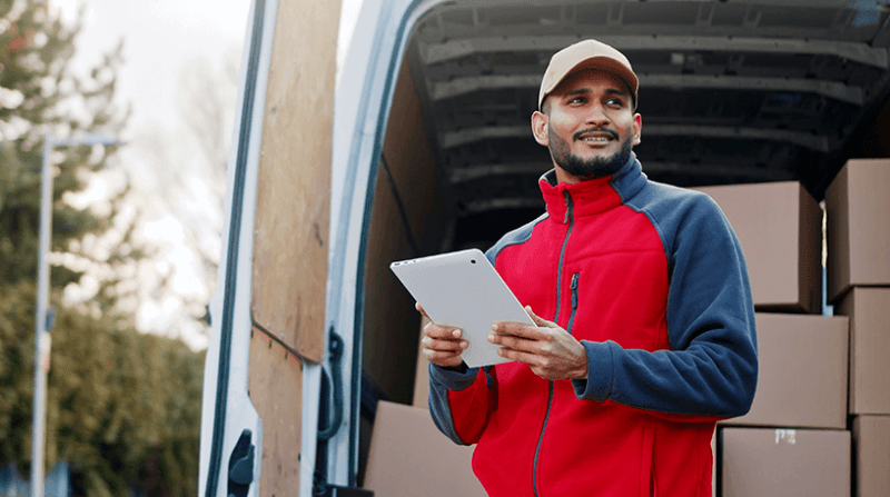 Male delivery driver holing an iPad in front of an open van