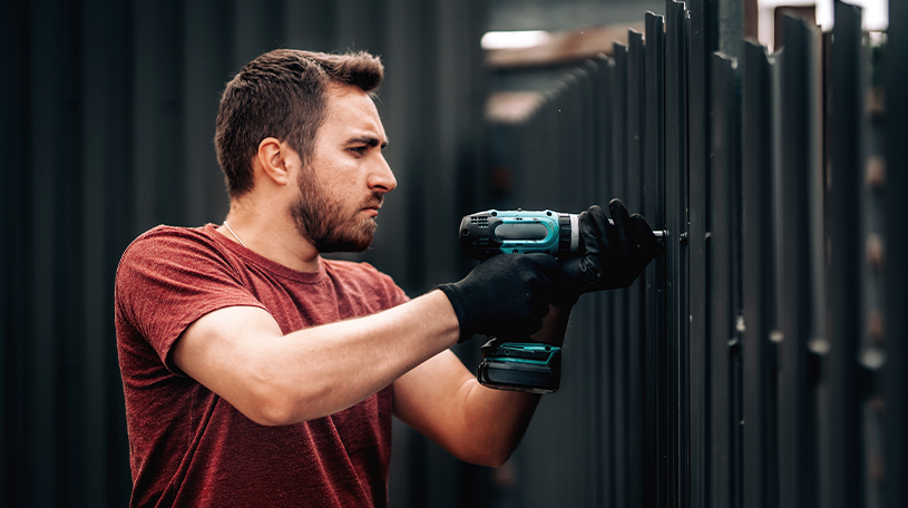 Workman drilling a black panel fence