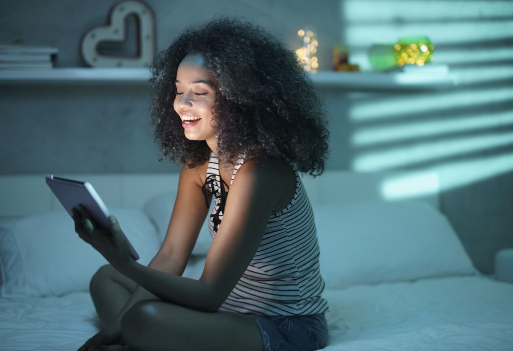 A woman sitting in her bedroom on a tablet