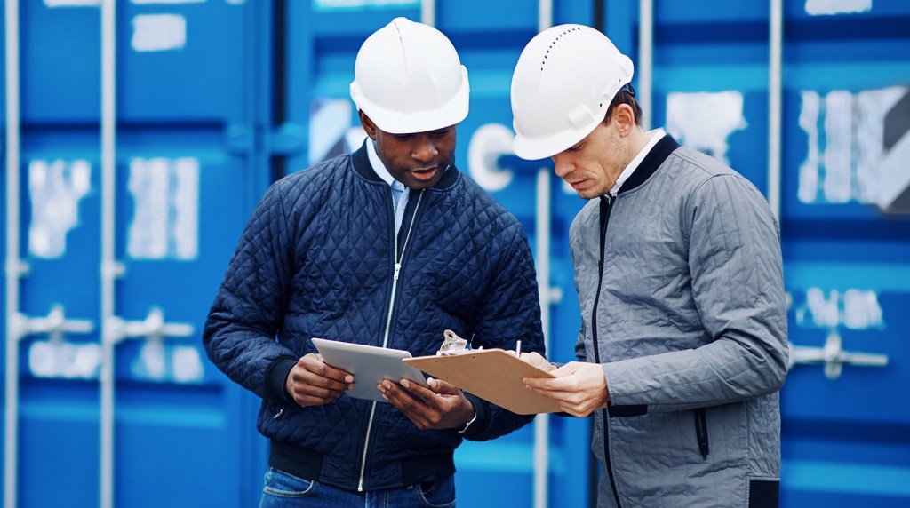 Two health and safety offers consulting assessment notes while on site and wearing protective clothing