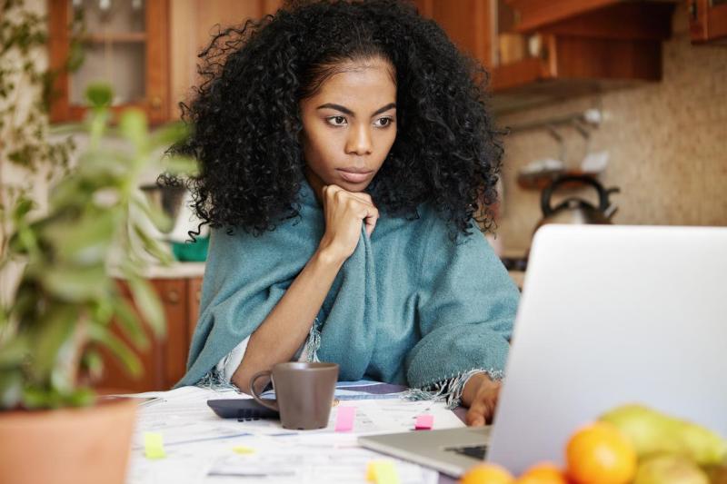 Woman using a laptop with papers and Post-Its on her desk