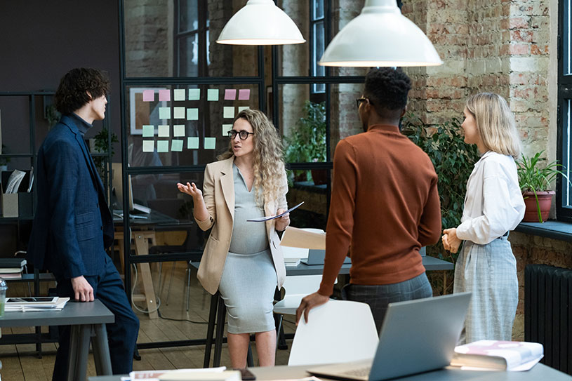 Pregnant businesswoman giving the tasks to employees before going to maternity leave