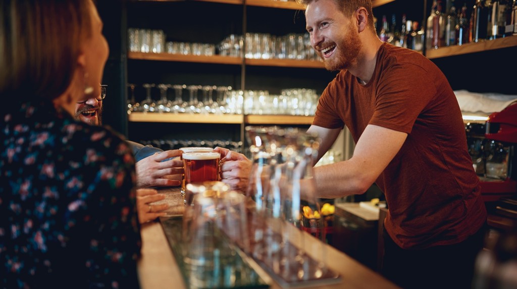 Pub barman serving beer to customers at the bar