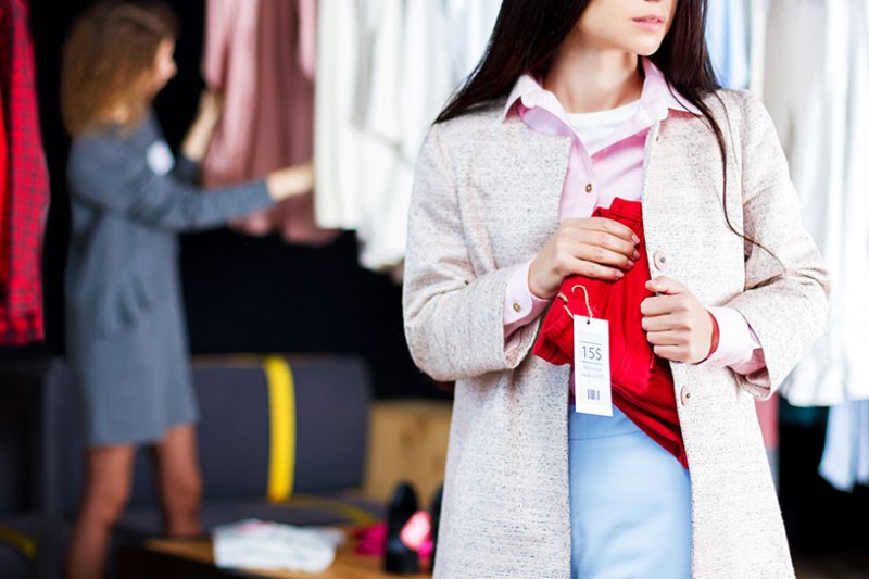 Woman stealing red jeans in small clothing shop