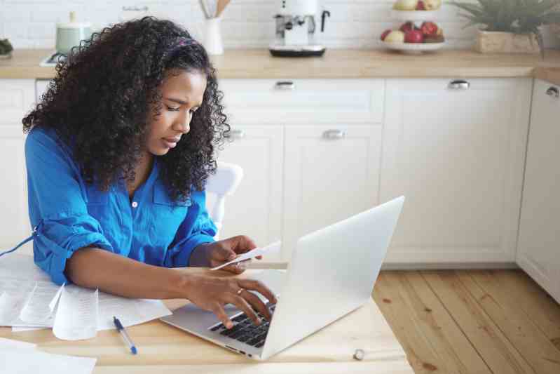 Woman looking at receipts and typing on laptop