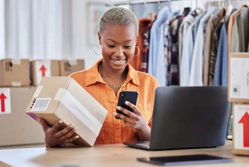 Clothing shop owner holding a package and looking at their phone.