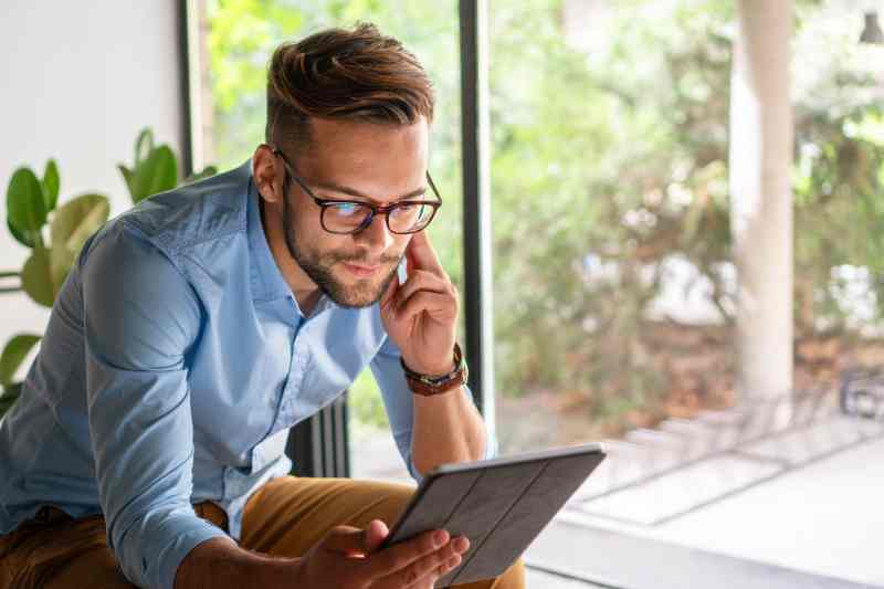 Man in glasses looking thoughtful using an iPad