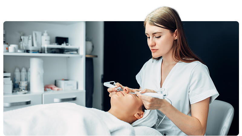 Beauty therapist performing a procedure on a client lying on a bed.