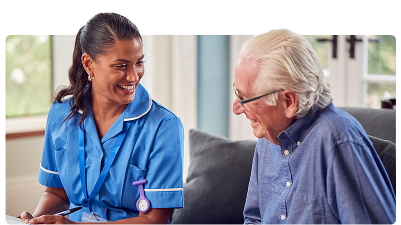 A carer in a blue uniform talking to an elderly man