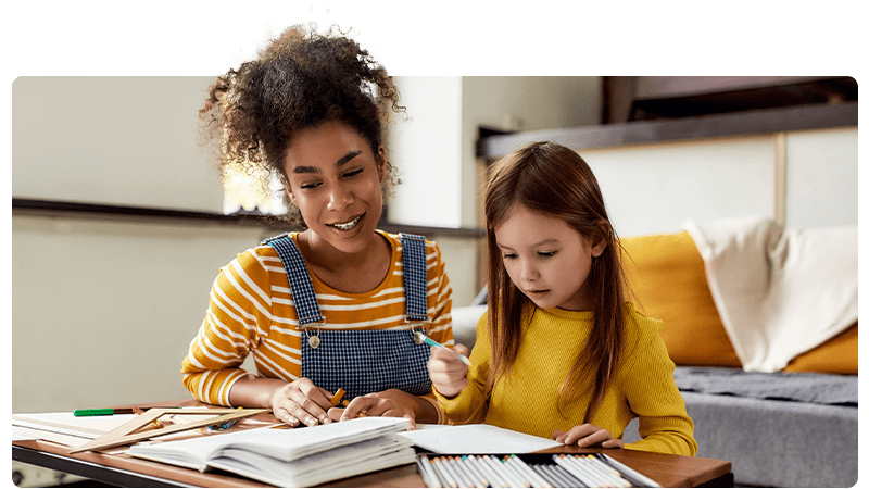 A childminder helping a little girl with her homework.