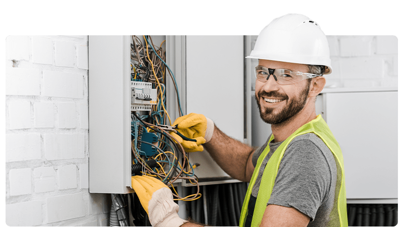 Electrician smiling at the camera whilst fixing wires in a fuse box