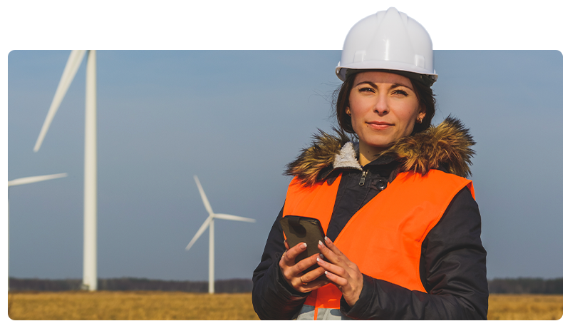 Environmental consultant in a high viz and hard hat in front of wind turbines.