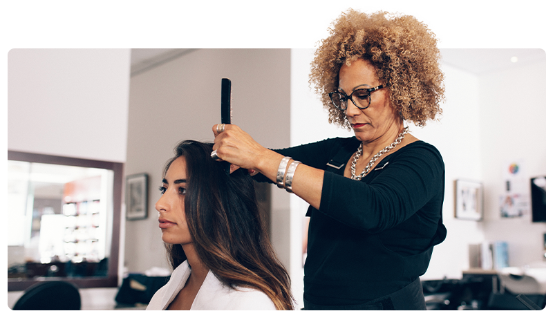 A hairdresser is styling a woman's hair in a hairdressers salon.