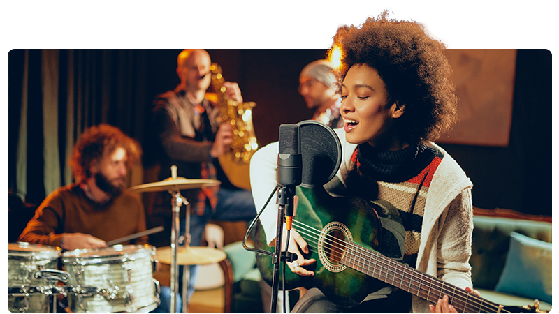 A musician playing the guitar and singing in front of other band members.