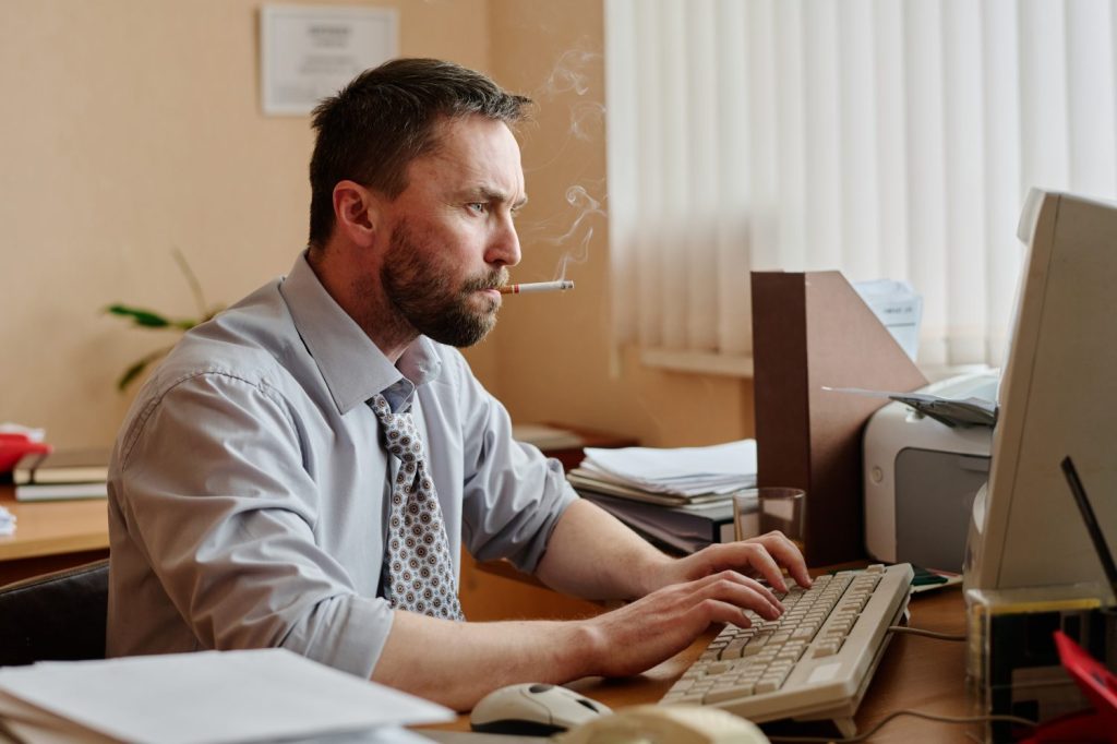 A man smoking inside working on a computer